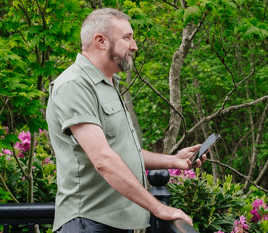 Man standing on a deck outside holding his phone and wearing a Dexcom sensor